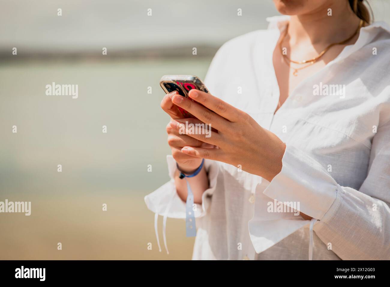 Nahaufnahme eines Mädchens Hände, die auf ihrem Smartphone neben einem See tippen Stockfoto