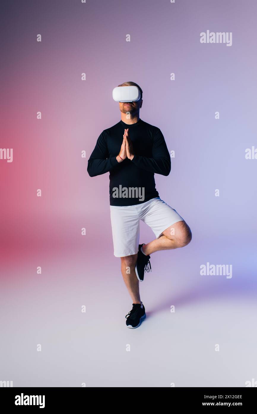 Ein Mann in einem schwarzen Hemd und weißen Shorts schlägt anmutig eine Yoga-Pose in einem Studio-Setting. Stockfoto