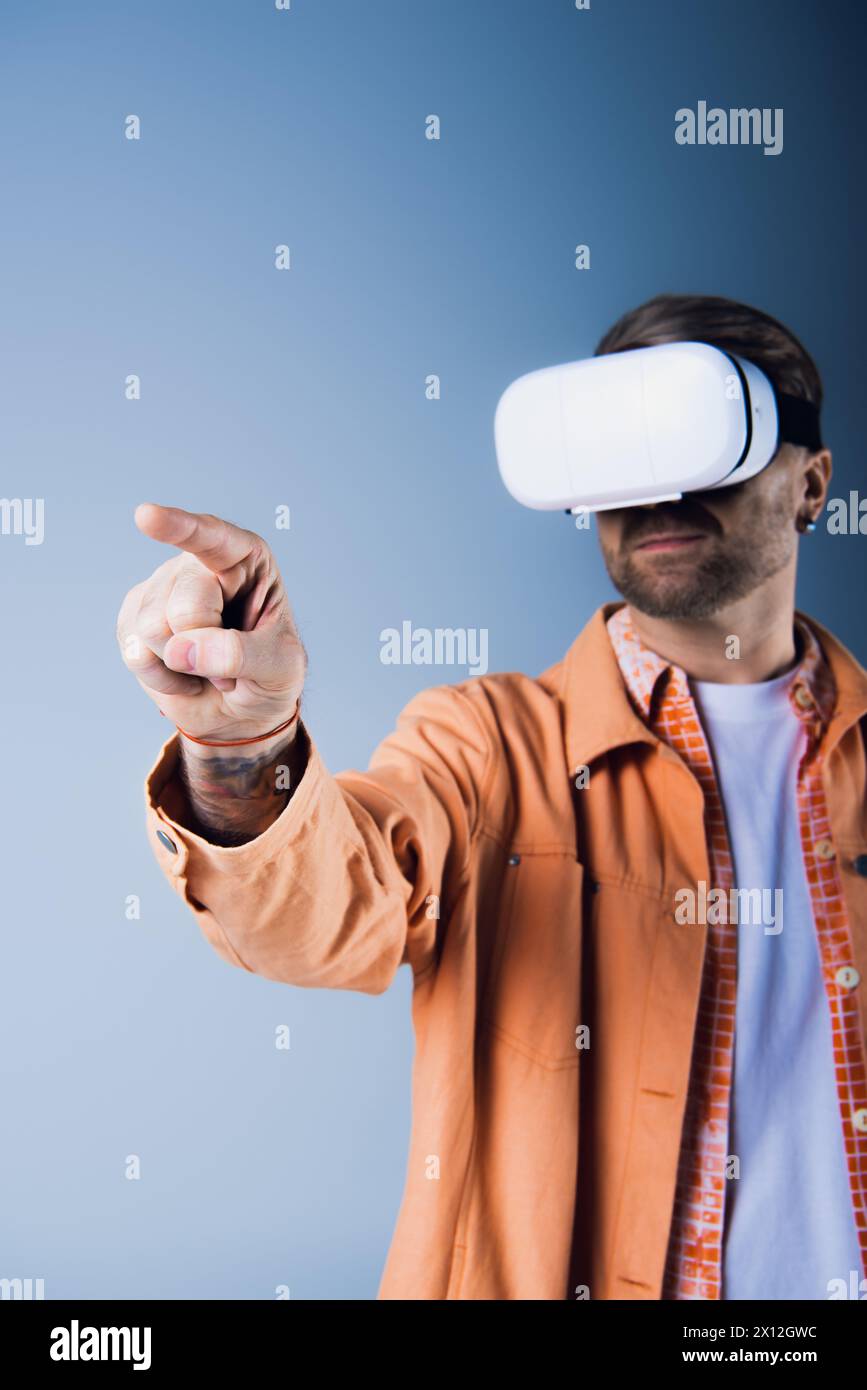 Ein Mann in einer orangefarbenen Jacke zeigt, während er ein VR-Headset in einer Studioumgebung trägt. Stockfoto