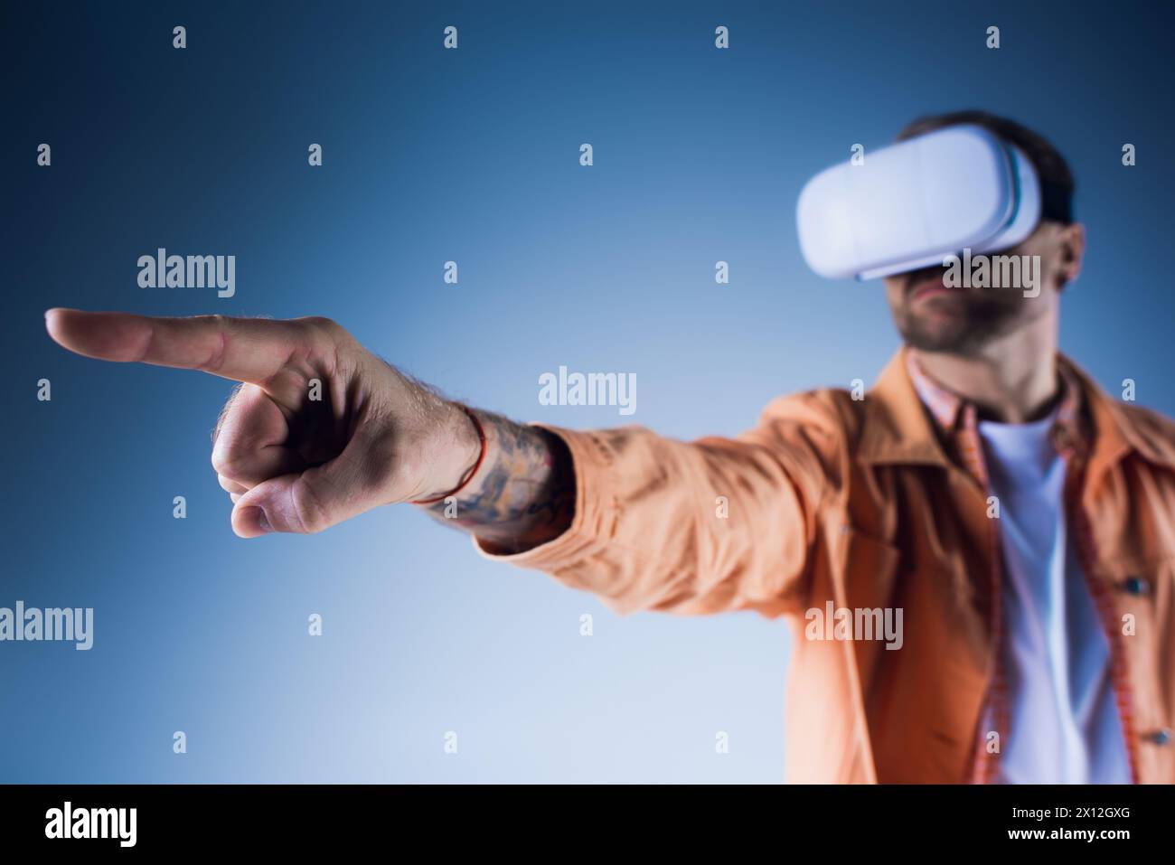 Ein Mann mit Hut zeigt auf etwas, während er in einem Virtual-Reality-Headset im Studio sitzt. Stockfoto
