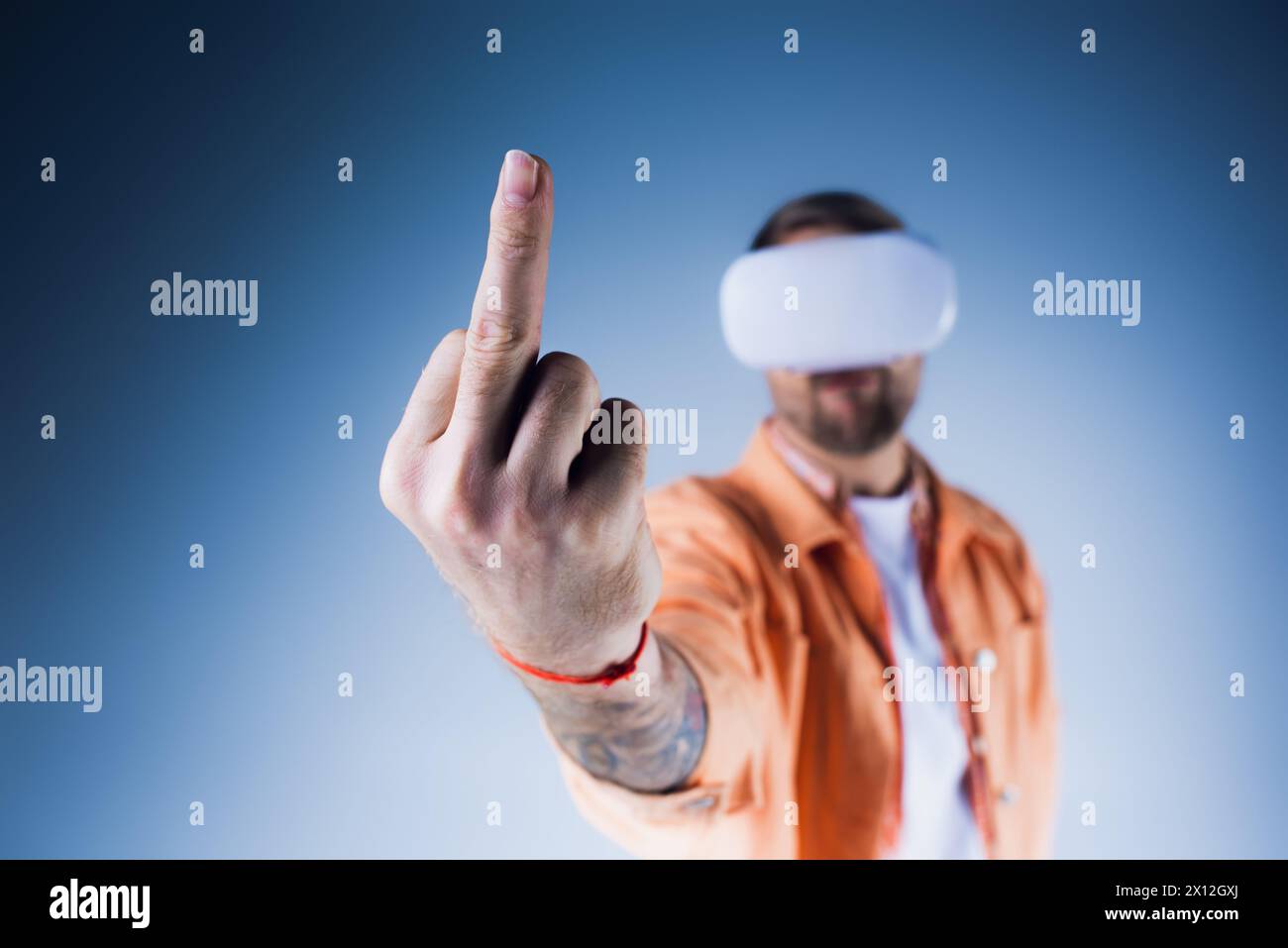 Ein Mann mit verbundenen Augen und einem VR-Headset zeigt selbstbewusst auf ein unsichtbares Ziel im Studio, Mittelfinger Stockfoto