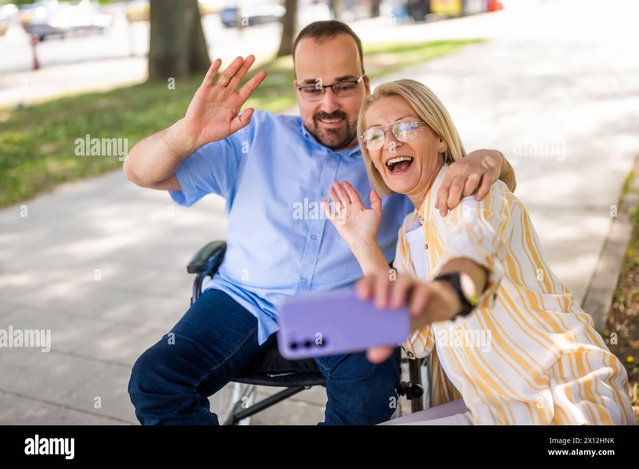 Ein Mann im Rollstuhl verbringt Zeit mit seiner Mutter im Park. Sie machen Selfie. Stockfoto
