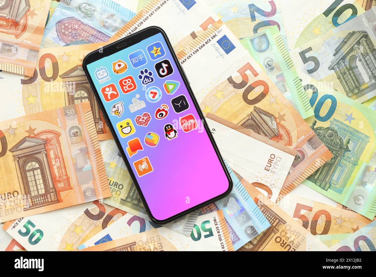 KIEW, UKRAINE - 1. APRIL 2024 auf vielen Euro-Geldscheinen finden Sie auf dem Smartphone-Bildschirm ein Symbol für asiatische Apps. IPhone-Display mit App-Logo mit Euro-Banknoten in europäischer Währung Stockfoto