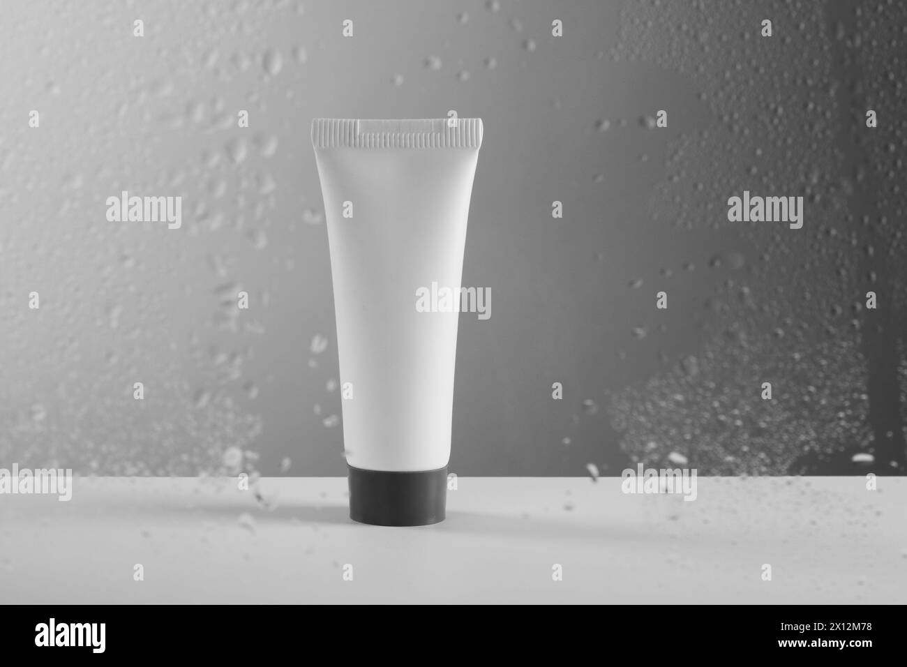 Röhrchen mit Feuchtigkeitscreme auf grauem Hintergrund, Blick durch nasses Glas Stockfoto