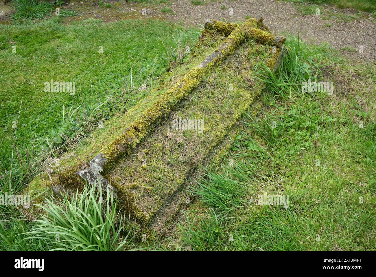 Grabstein mit Gras und Moos bedeckt, kreuzförmig geschnitzt. Stockfoto