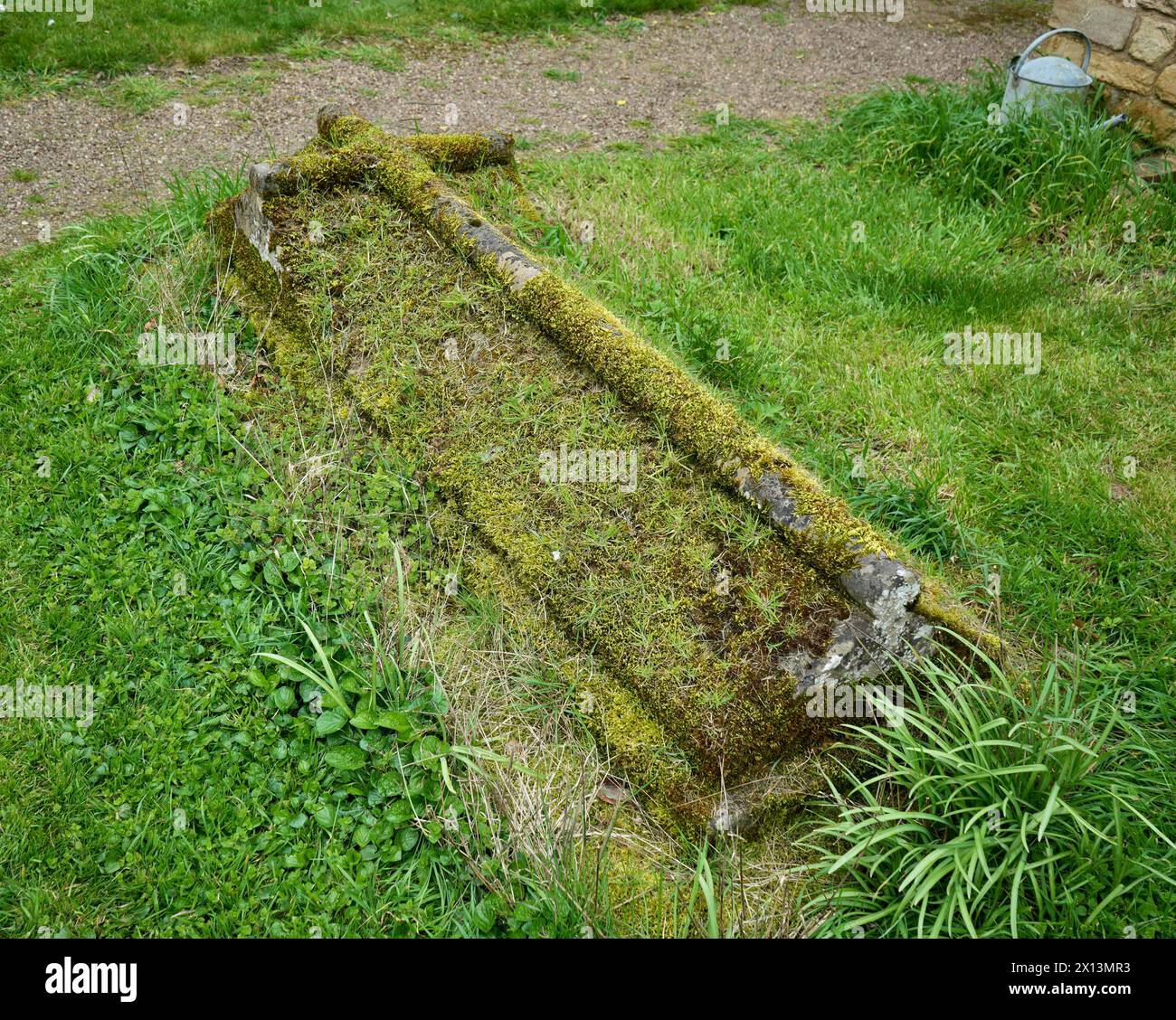 Grabstein mit Gras und Moos bedeckt, kreuzförmig geschnitzt. Stockfoto