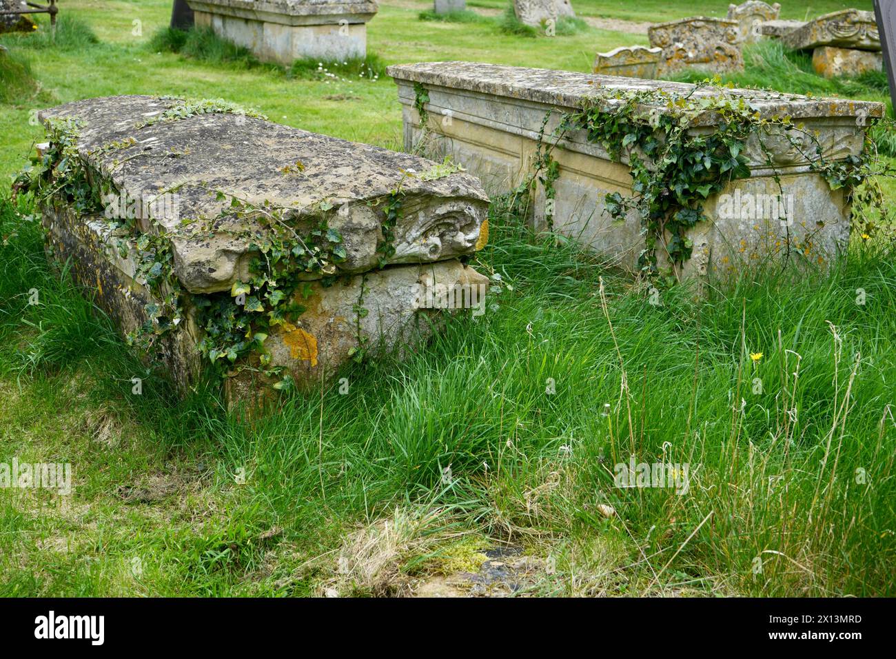 Alte Ivy bedeckte Gräber in St. Peter und St. Paul Churchyard, einer Dorfkirche aus dem 12. Jahrhundert. Stockfoto