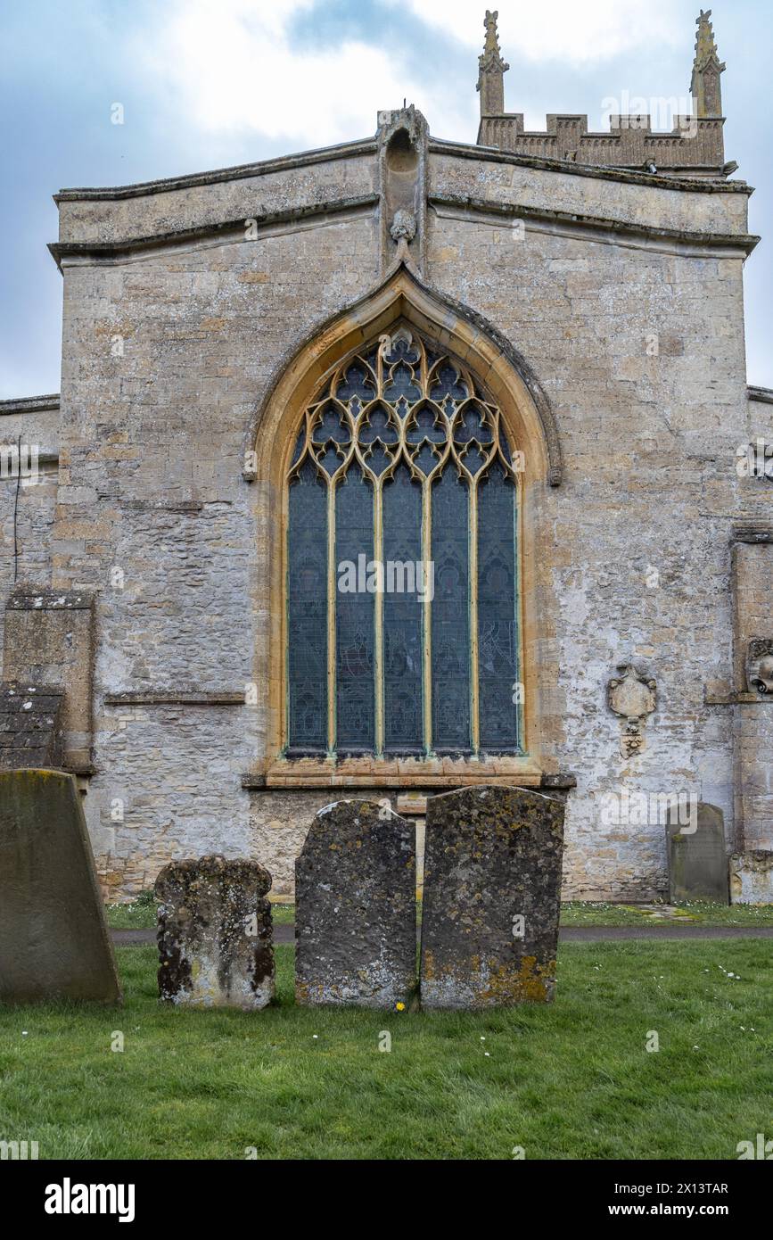 Ein großes bogenförmiges Buntglasfenster, das durch ein Drahtgeflecht geschützt wird, in der St Edwards Church, Stow on the Wold, den Cotswolds, England. Stockfoto