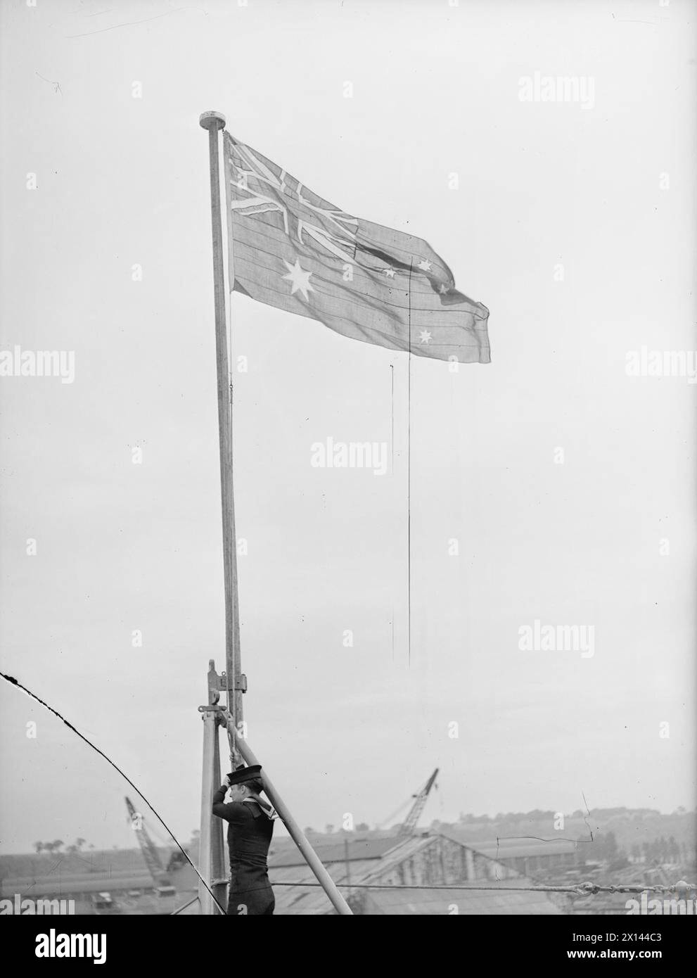 Der County Class Kreuzer HMS Shropshire wurde am 25. Juni 1943 in Chatham von Admiral Sir George D’Oyly Lyon, KCB, Oberbefehlshaber, Nore, übergeben und ersetzte die HMAS Canberra. versunken vor den Salomonen. Eine Signaleinstufung schiebt den Blauen Fähnrich während der Zeremonie an den Jackstab. Stockfoto