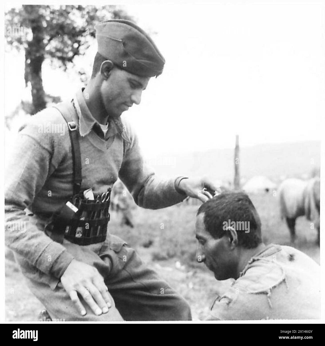 Ein indischer Friseur beim Royal Indian Army Service Corps gibt einen Haarschnitt mit Utensilien, die in einem Ledergürtel getragen werden. Stockfoto