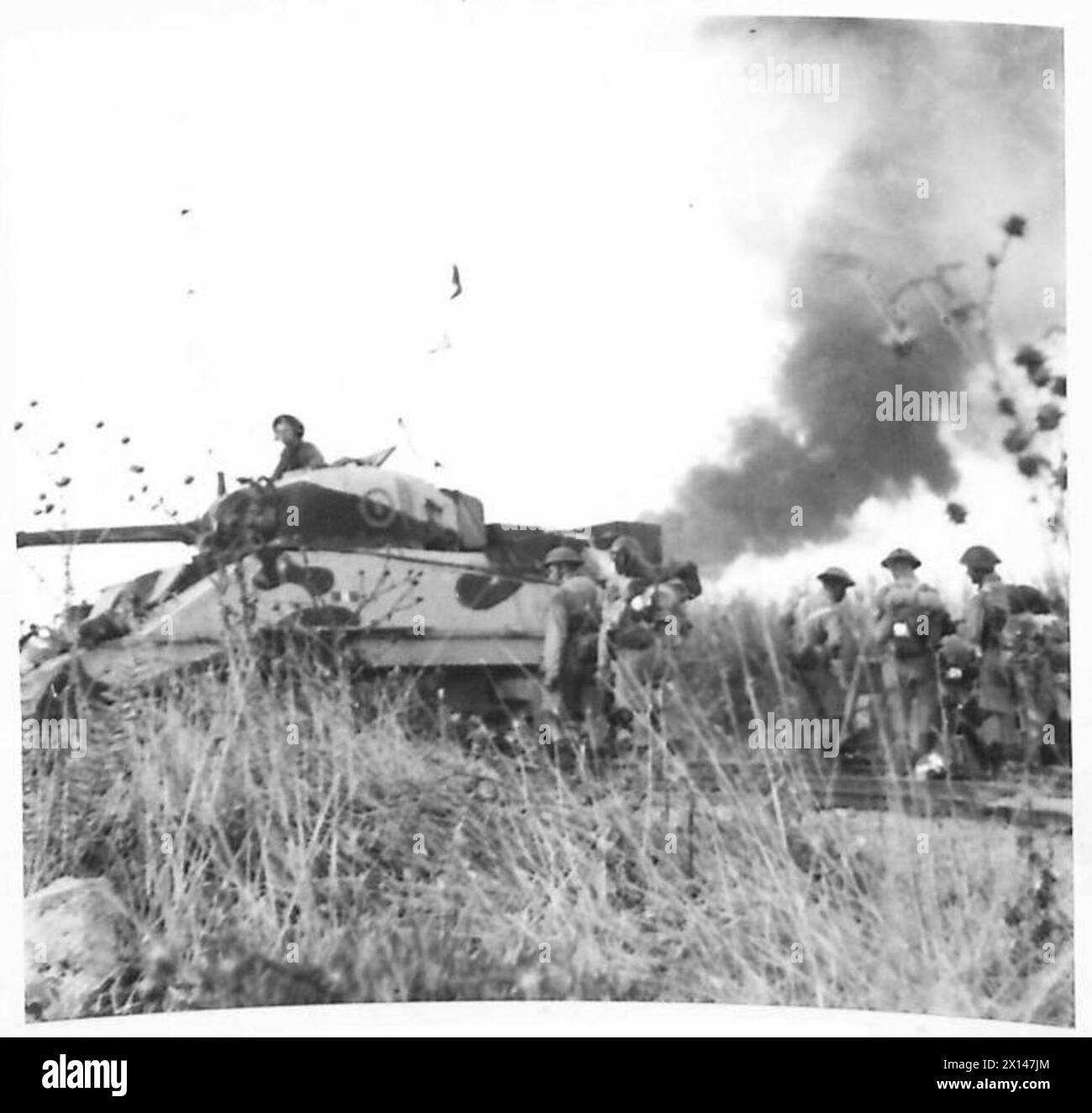 Ein Sherman-Panzer stürzt auf der Straße nach Battipaglia vor, als während der Landung der Fünften Armee in Italien Rauch von einem brennenden Munitionsschiff in der Bucht von Salerno aufsteigt. Stockfoto