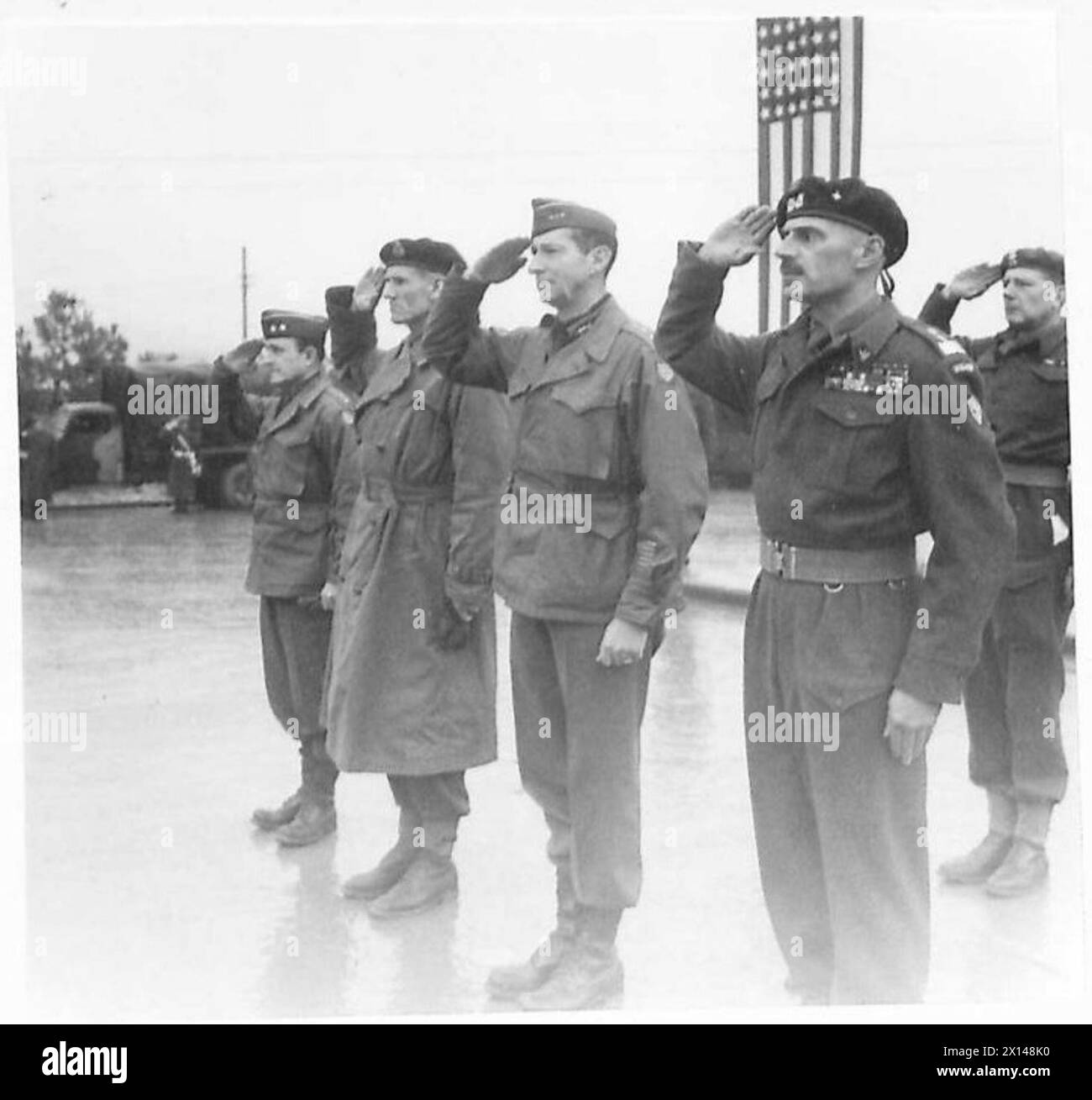 DIE ALLIIERTEN ARMEEN IM ITALIENISCHEN FELDZUG, 1943-1945: General Richard McCreery (2. Von links), General Mark Clark (Mitte) und General Władysław anders (1. Von rechts), die während des Spiels einer Nationalhymne den Gruß nahmen. Leutnant Eugeniusz Lubomirski, Adjutant von General anders, ist in der zweiten Reihe und grüßt. Foto, aufgenommen während Generäle Clark und McCreery im Hauptquartier des 2. Polnischen Korps in Predappio. General Clark wurde während dieses Besuchs auch mit Virtuti Militari dekoriert. Ein AFPU-Kameramann in Schneebarntfarbe filmt polnische Infanteristen, die von einer Patrouille zurückkehren, Stockfoto