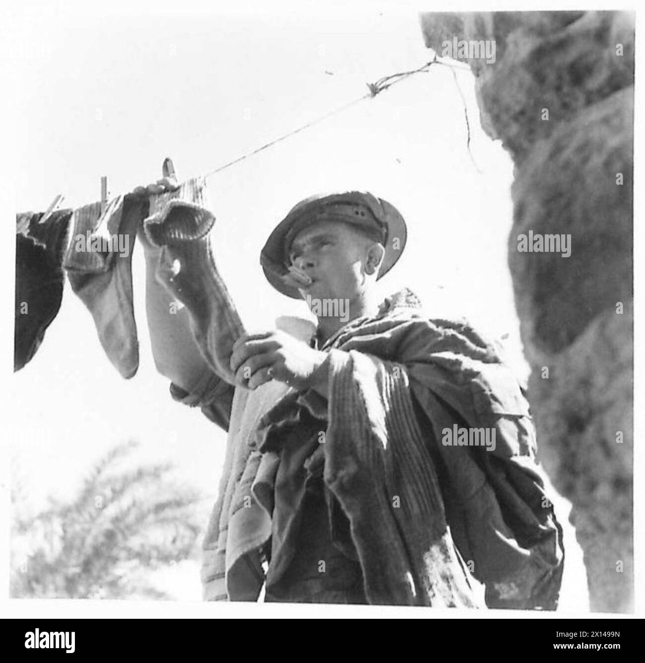 Ein Soldat hängt seine Wäsche zum Trocknen auf, benutzt seinen Mund, um die Stifte zu halten, während des Waschtages auf dem Feld. Stockfoto