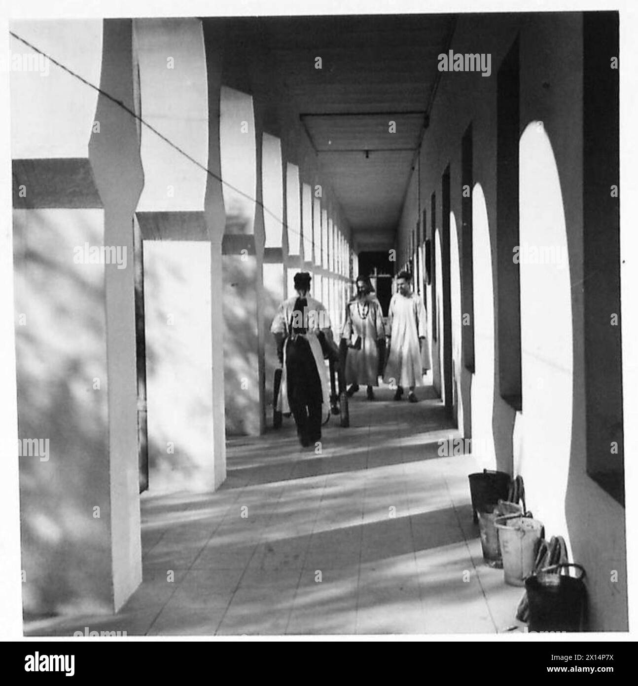 Medizinisches Personal geht durch den Kreuzgang zum Operationssaal einer nordafrikanischen Unfallstation und trifft auf zwei Mitglieder der Weißen Väter. Stockfoto