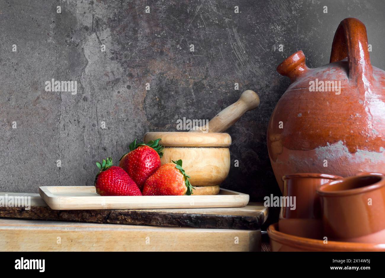 Erdbeeren auf einem Holztablett neben einem alten Botijo und anderen Keramik- und Holzutensilien Stockfoto