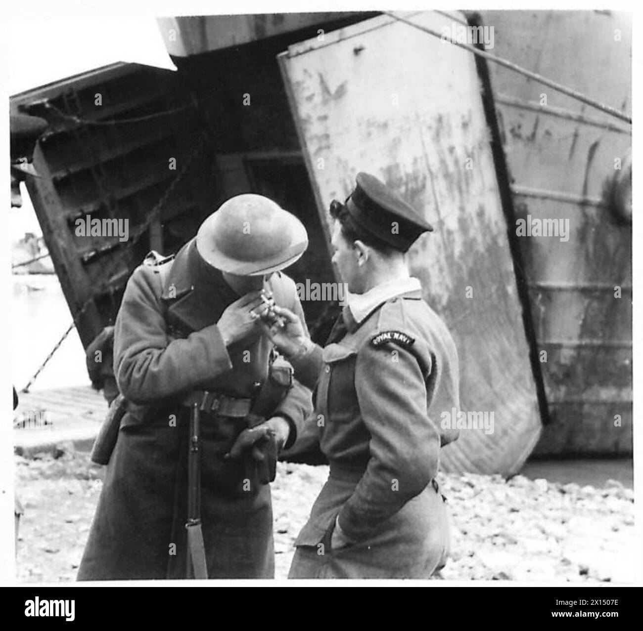 Private Johnson, Verstärkung der Queens, erhält ein Licht für seine Zigarette von einem Marineoffizier am Hafen des Anzio Brückenkopfes der Fünften Armee in Italien, beobachtet von britischen Armeepersonal. Stockfoto