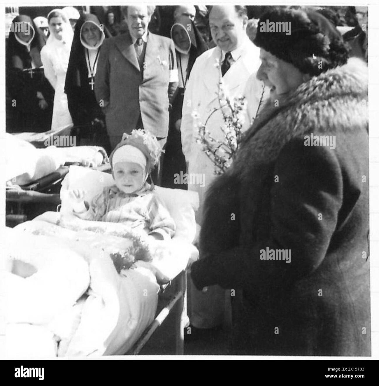 Königin Wilhelmina von den Niederlanden interagiert mit einem Kind, das während der Belagerung von Venlo verletzt wurde, während sie Holland besucht, begleitet von britischen Armeeangehörigen der 21. Armeegruppe. Stockfoto