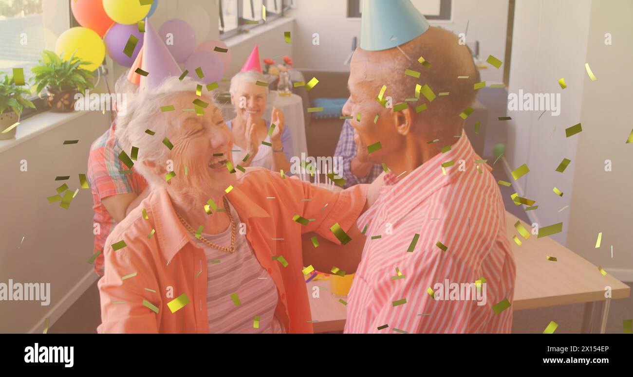 Goldenes Konfetti, das gegen das kaukasische Seniorenpaar fällt, das während der Geburtstagsfeier zusammen tanzt Stockfoto