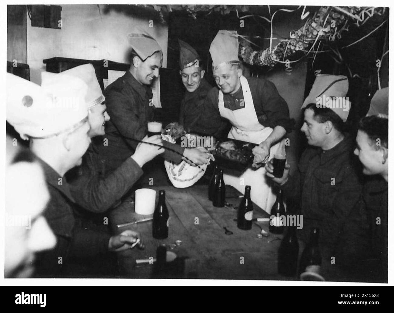 Ein Koch serviert zubereitete Vögel zu Weihnachten in einem dekorierten Militärchaos vor Truppen mit Papierhüten. Stockfoto