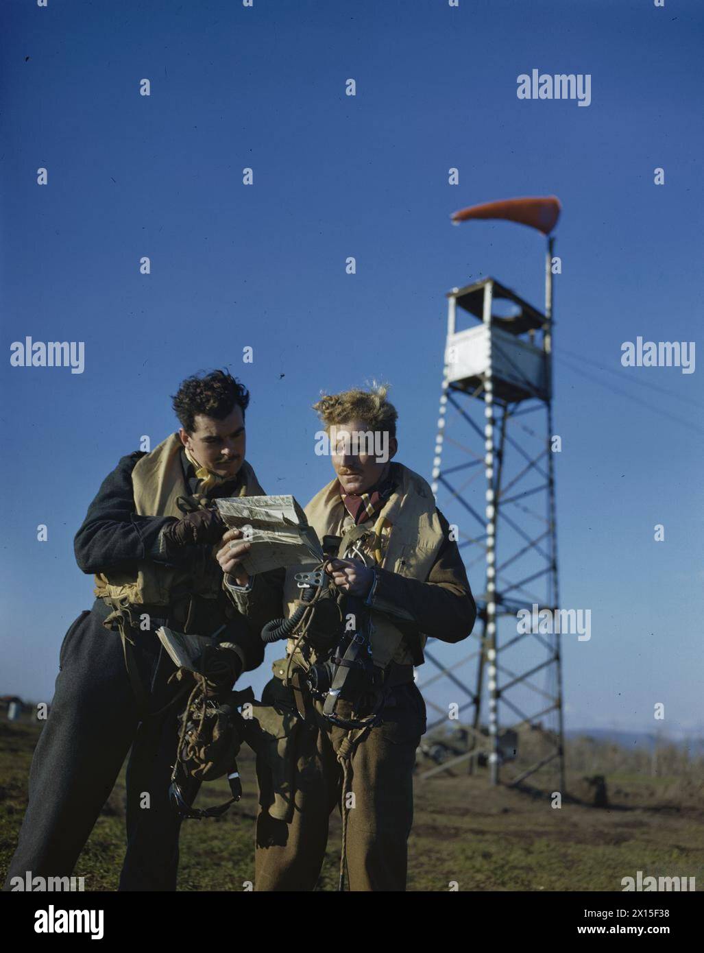 SUPERMARINE SPITFIRE DER ROYAL AIR FORCE IN ITALIEN, JANUAR 1944: Zwei Supermarine Spitfire-Piloten der No 241 Squadron, der Flying Officer J S B Reynolds (rechts) und der Flying Officer W R B McMurray schauen sich eine Karte in Italien an. Eine Windsocke auf einem Aussichtsturm ist im Hintergrund der Royal Air Force, Group, 241 zu sehen Stockfoto