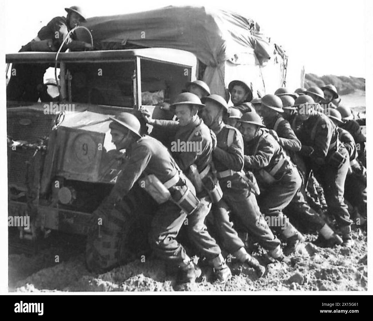 Die Truppen unterstützen einen Lkw, der sich bei einer Landung der Alliierten südlich von Rom in weichem Schlamm feststeckt, und setzen dabei koordinierte Anstrengungen ein, um das Fahrzeug zu bewegen. Stockfoto