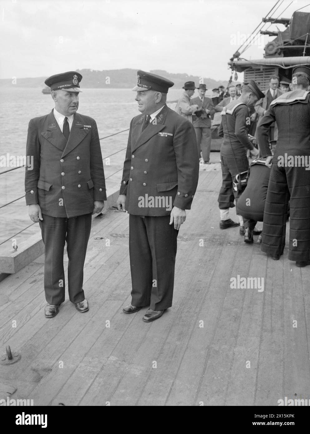 HMAS AUSTRALIA IN PLYMOUTH AN REFIT. AM 1. JULI 1945 TRAF PLYMOUTH, HMAS AUSTRALIA, EIN HOCHRANGIGES SCHIFF DER AUSTRALISCHEN MARINE, DAS VOR LEYTE VON EINEM JAPANISCHEN SELBSTMORDATTENTÄTER SCHWER BESCHÄDIGT WURDE, IN PLYMOUTH EIN, UM DORT UMZUBAUEN. DIE RT HON S M BRUCE, HOHER KOMMISSAR FÜR AUSTRALIEN, BEGLEITET VON ADMIRAL SIR RALPH LEATHAM, C IN C PLYMOUTH, BEGRÜSSTE DEN KOMMANDANTEN DES SCHIFFES, CAPTAIN J M ARMSTRONG, DSO, RAN UND DIE CREW BEI DER ANKUNFT. - Auf der rechten Seite befindet sich CPO G L Rosbrook, RAN, der sich 1902 seinem ersten Schiff in Plymouth angeschlossen hat. Er ist gerade zum ersten Mal seit 12 Jahren in AUSTRALIEN zurückgekehrt Stockfoto