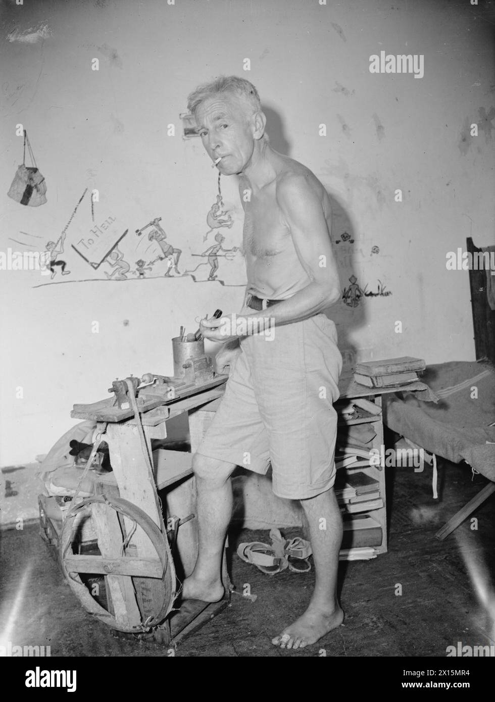 IM STANLEY INTERNIERUNGSLAGER, HONGKONG. AUGUST UND SEPTEMBER 1945. - Der älteste Bewohner des Lagers, Mr. A Raven, 70 Jahre alt, ein Architekt aus Yorkshire, demonstriert seine selbstgebaute Drehmaschine, die er aus Stücken der Japanischen Garde und Schrott im Lager gemauert hat. Die Drehmaschine wurde speziell für Eheringe aus 10 Cent Hongkong-Stücke für verheiratete Frauen hergestellt, die gezwungen waren, ihre goldenen Ringe für wichtige Toilettenartikel und Lebensmittel zu verkaufen. Andere Artikel, die von Mr. Ravens Drehmaschine geliefert wurden, waren Knöpfe für die selbstgemachte Kleidung, die Internierten aus Stücken von r Stockfoto