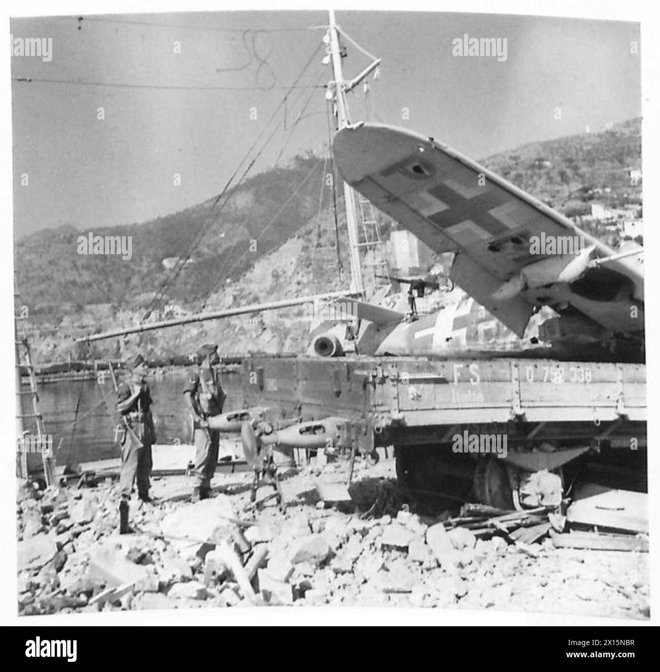 Britische Truppen der Fünften Armee dringen in Salerno ein, während ein deutsches Kampfflugzeug auf einem Eisenbahnwaggon in den Docks positioniert wird, was die städtischen Operationen und Besatzungsaktivitäten hervorhebt. Stockfoto