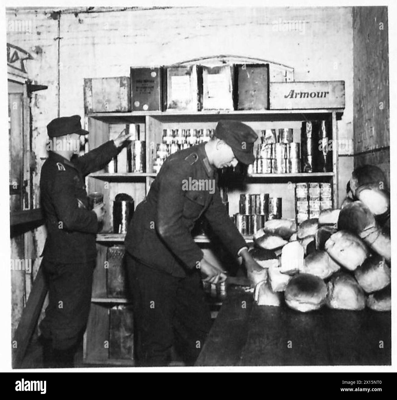Der Lagerführer kontrolliert die täglichen Rationen, während der Lagerführer unter Aufsicht der britischen Armee, der 21. Armeegruppe, Weißbrot in rationierte Portionen teilt. Stockfoto
