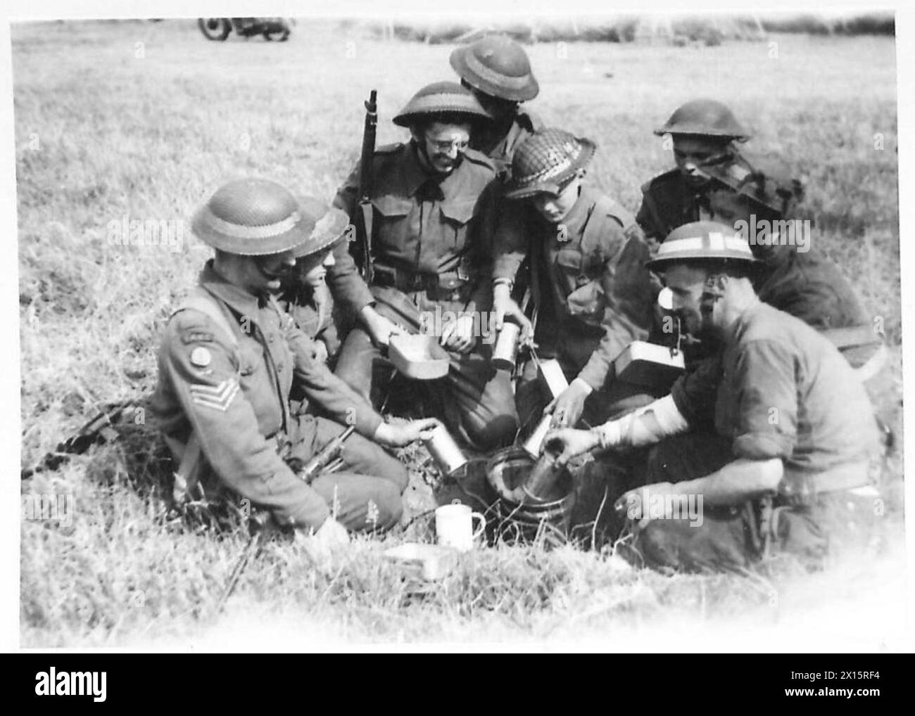 WIE DIE TRUPPEN IN DER NORMANDIE LEBEN - Männer sammeln normalerweise Rationen in kleinen Gruppen. Hier sind ein paar Männer mit „Dixie“ und kleinem Feuer in einem Schlitzgraben, die ihre Dosen „Steak and Kidney Pudding“ von der britischen Armee „Compo Pack“, 21. Armeegruppe, aufwärmen Stockfoto