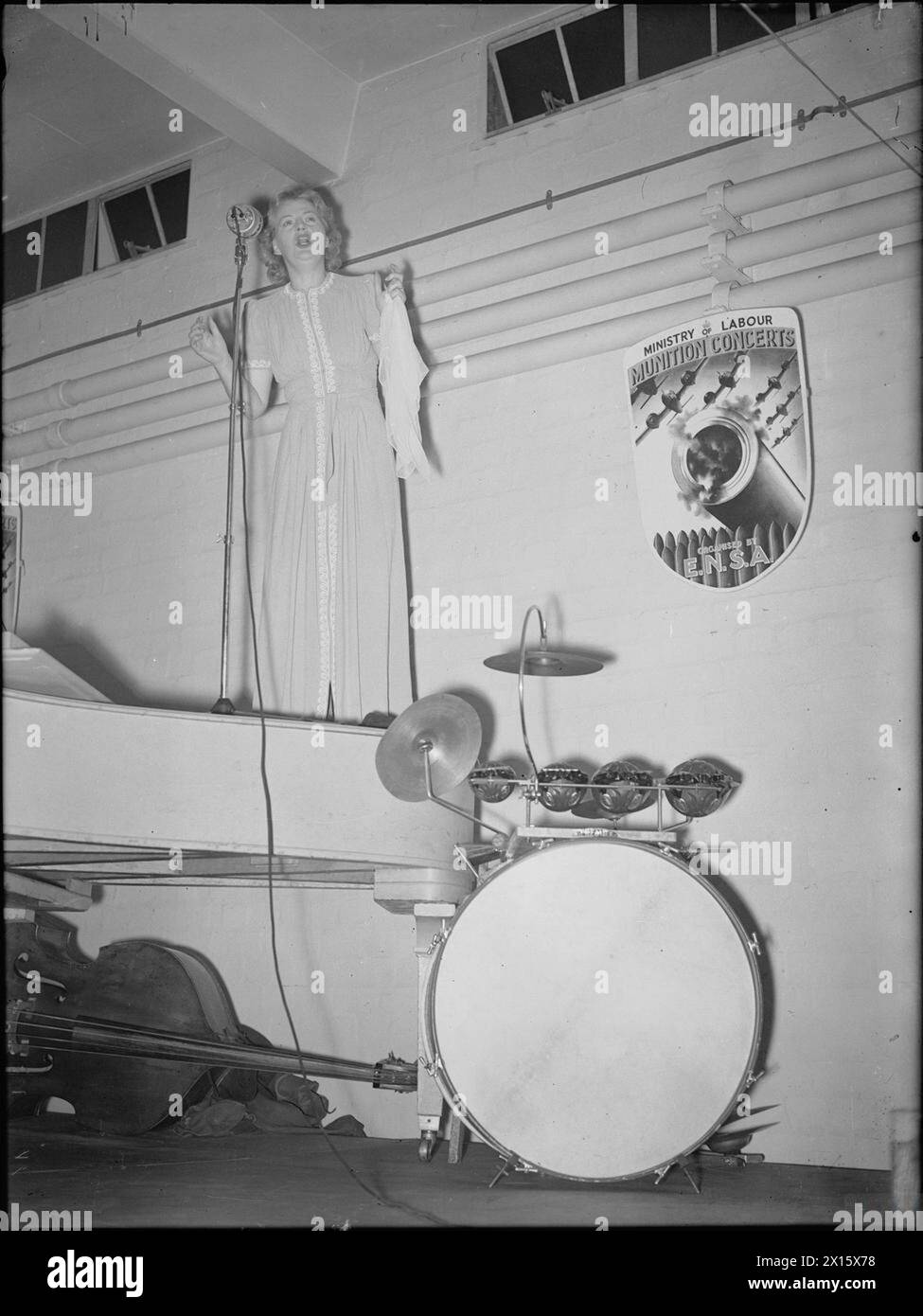 Gracie Fields tritt 1941 auf einem Flügel in einer Munitionsfabrik in Großbritannien auf und unterhält Fabrikarbeiter mit sichtbarem Schlagzeug und Kontrabass. Stockfoto Gracie Fields tritt 1941 auf einem Flügel in einer Munitionsfabrik in Großbritannien auf und unterhält Fabrikarbeiter mit sichtbarem Schlagzeug und Kontrabass. Stockfoto