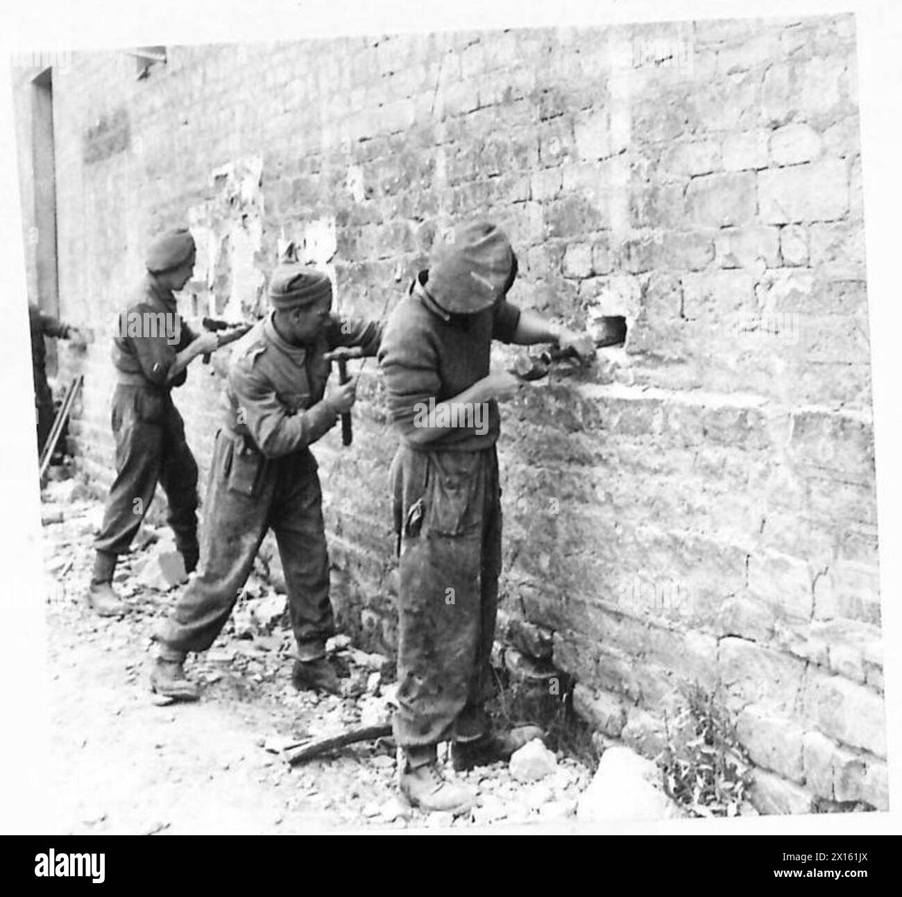 Royal Engineers bereiten Sprengladungen vor, indem sie Löcher in die Wände eines Hauses bohren, während sie ein verwüstetes französisches Dorf im Rahmen der Operationen der britischen Armee räumen. Stockfoto