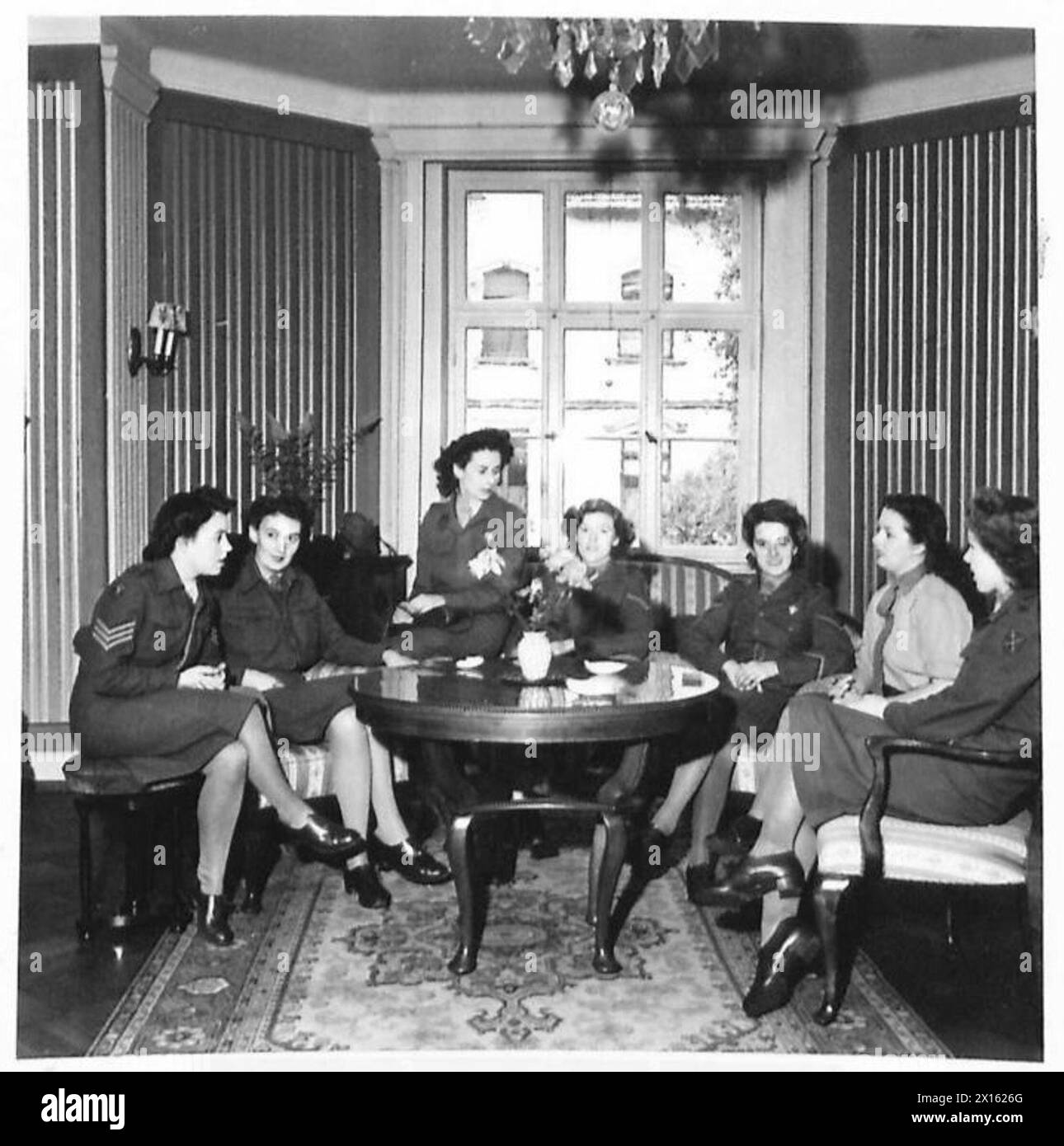 Sieben Mitglieder des Auxiliary Territorial Service unterhalten sich um einen Tisch in ihrem Aufenthaltsraum in Deutschland, darunter Sergeant K. Munday, Corporal O. Young und L/Corporals D. Merrison, G. Willcox, J. Farlow, J. Parfitt und Private L. Fox während der Operationen der britischen Armee mit der 21. Armee. Stockfoto