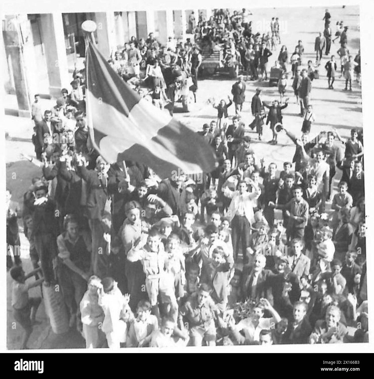 Britische Truppen dringen in Patras ein, während lokale Bürger während der Befreiungsoperationen die Nationalflagge anfeuern und schwenken. Stockfoto