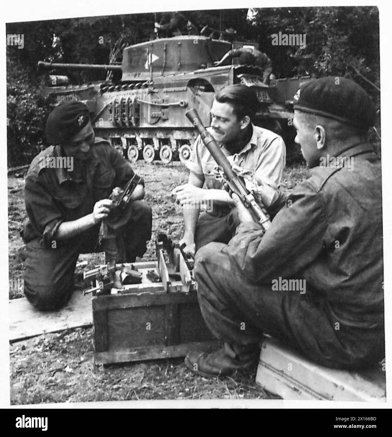 Die Besatzung eines Churchill-Panzers führt Wartungsarbeiten an dem Fahrzeug durch; zwei Soldaten reinigen das Maschinengewehr 7,92 Besa, während der Panzerkommandant überwacht, um sicherzustellen, dass alle Waffen einsatzbereit sind. Stockfoto