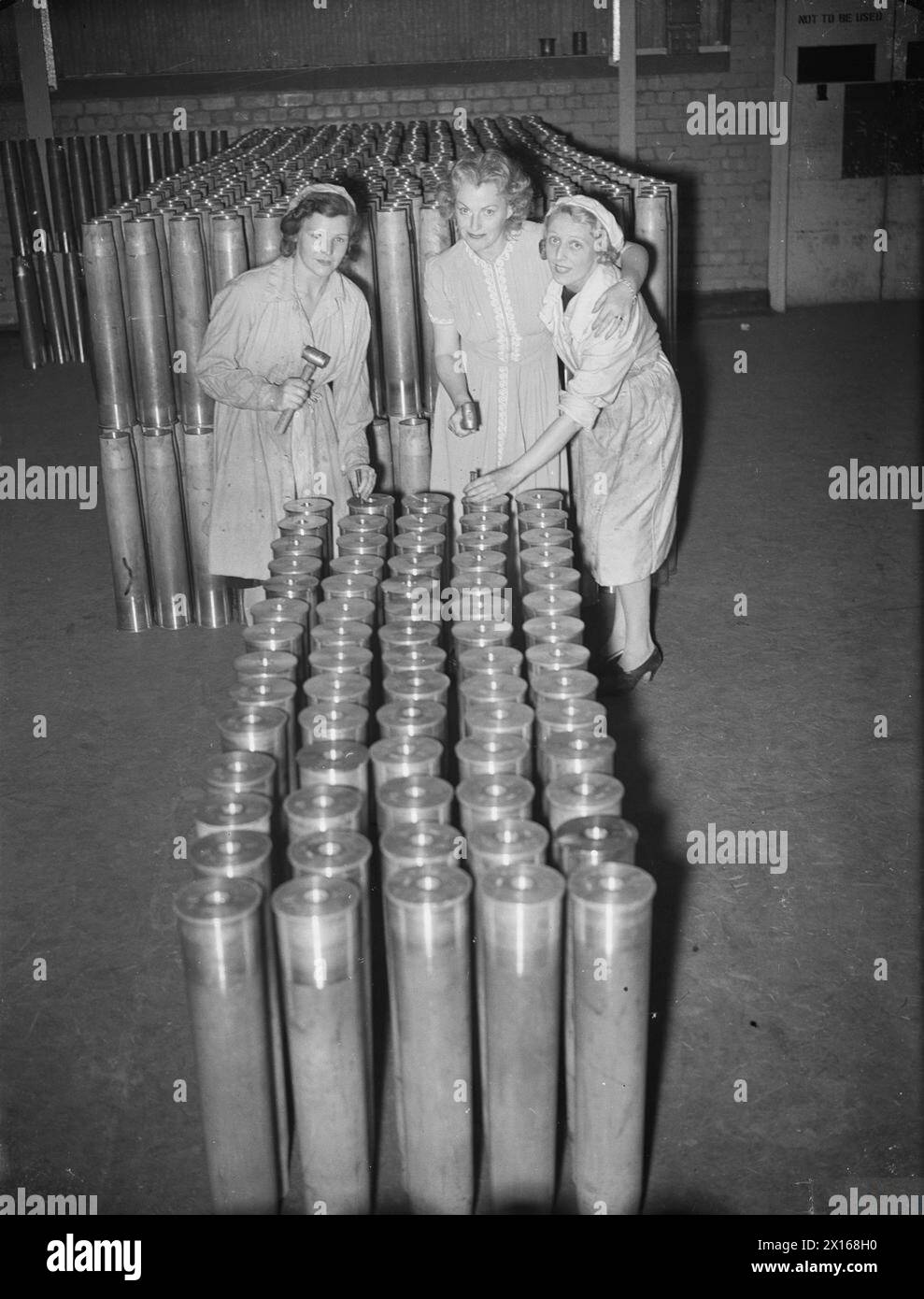 Gracie Fields besucht 1939-1945 eine britische Kampfmittelfabrik, um Arbeiterinnen beim Stempeln von Granatkästen zu helfen und an einem von der ENSA organisierten Munitionskonzert des Arbeitsministeriums teilzunehmen. Stockfoto Gracie Fields besucht 1939-1945 eine britische Kampfmittelfabrik, um Arbeiterinnen beim Stempeln von Granatkästen zu helfen und an einem von der ENSA organisierten Munitionskonzert des Arbeitsministeriums teilzunehmen. Stockfoto