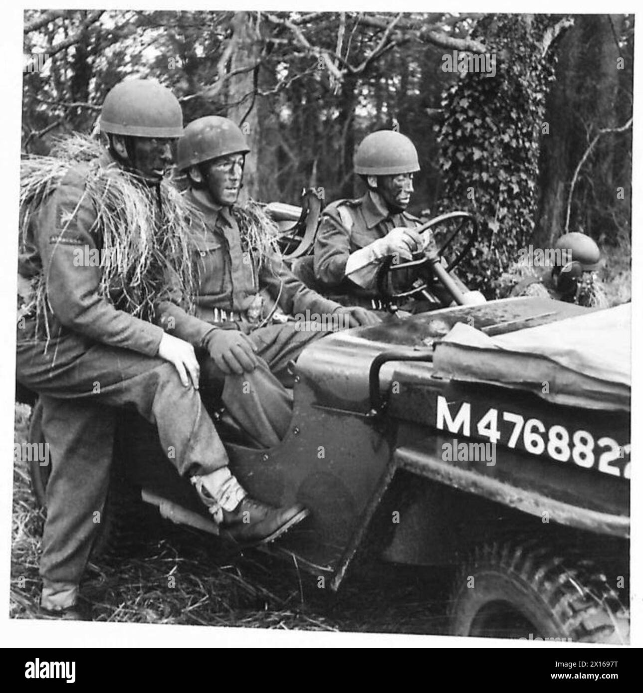 Fallschirmjäger mit Kriegsfarbe und Kopfbedeckungen aus Grasstroh ziehen durch einen Wald, während sie von Kriegskorrespondenten besucht werden. Stockfoto