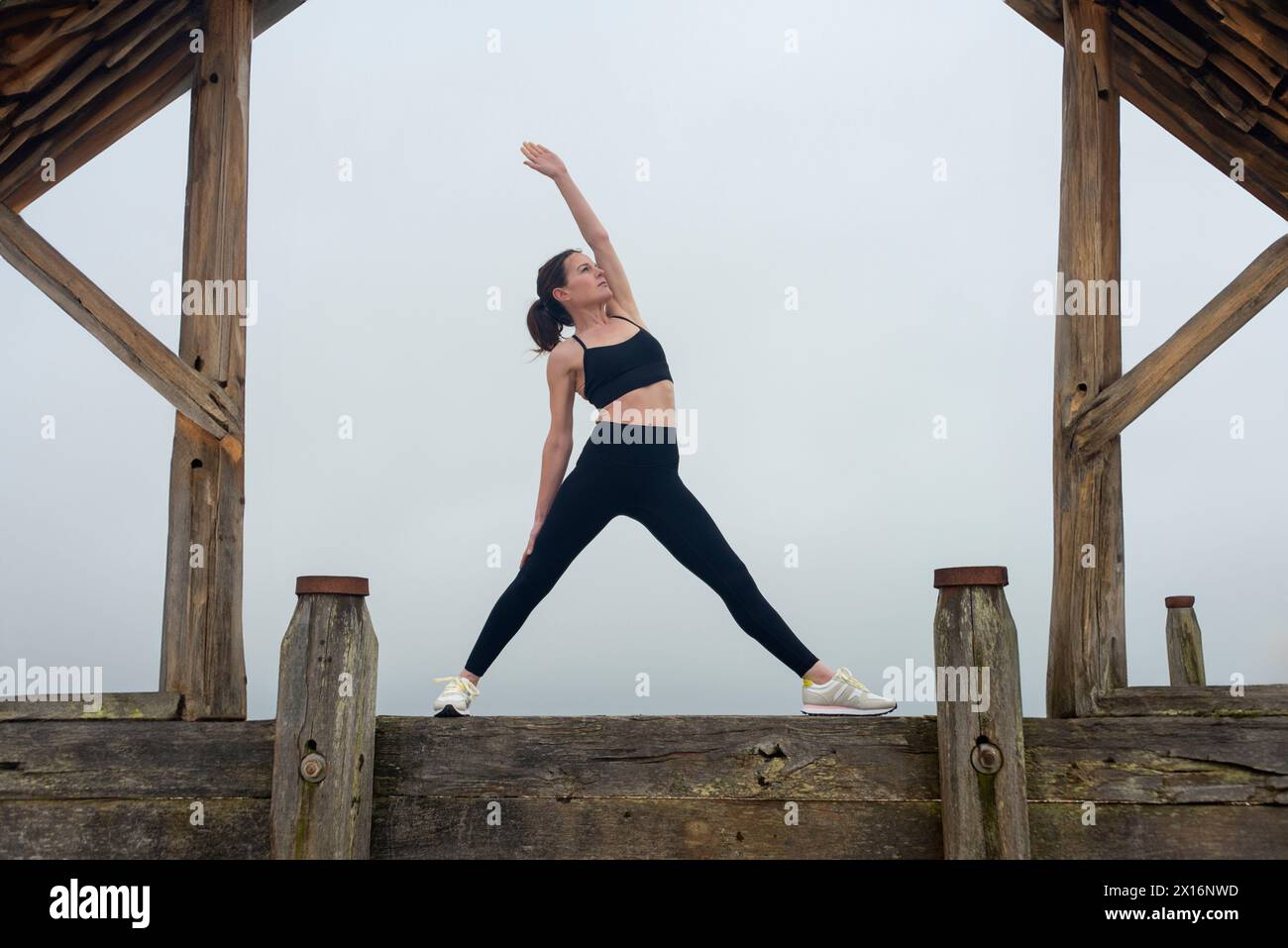 Sportliche Frau, die eine Yoga-Pose macht, draußen bei einem Holzgebäude Stockfoto