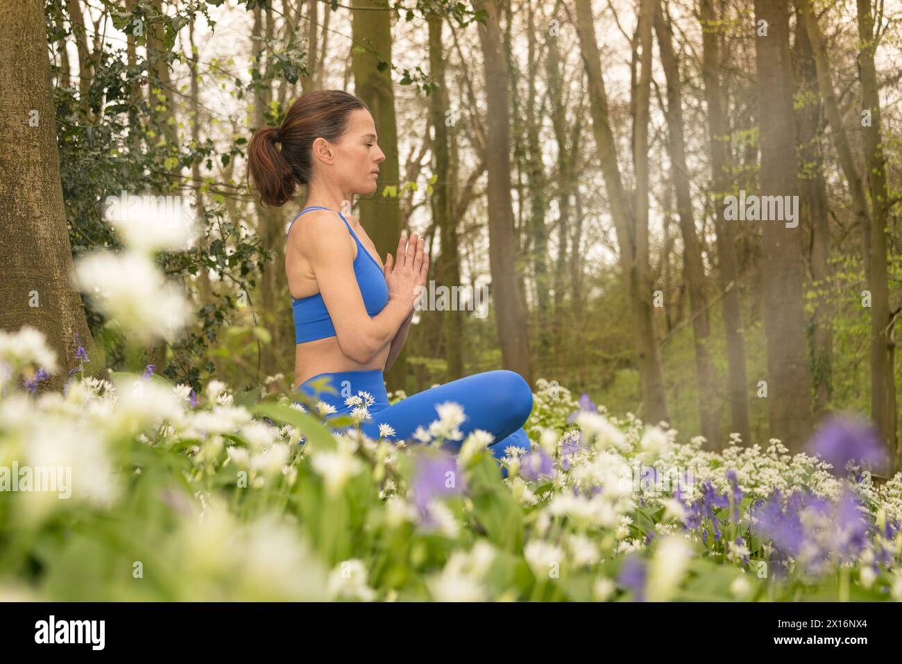 Frau, die in der Natur meditiert, wilder Knoblauch- und Blauglockenwiese und Wald. Fitness-Konzept für Frühling und Sommer. Stockfoto