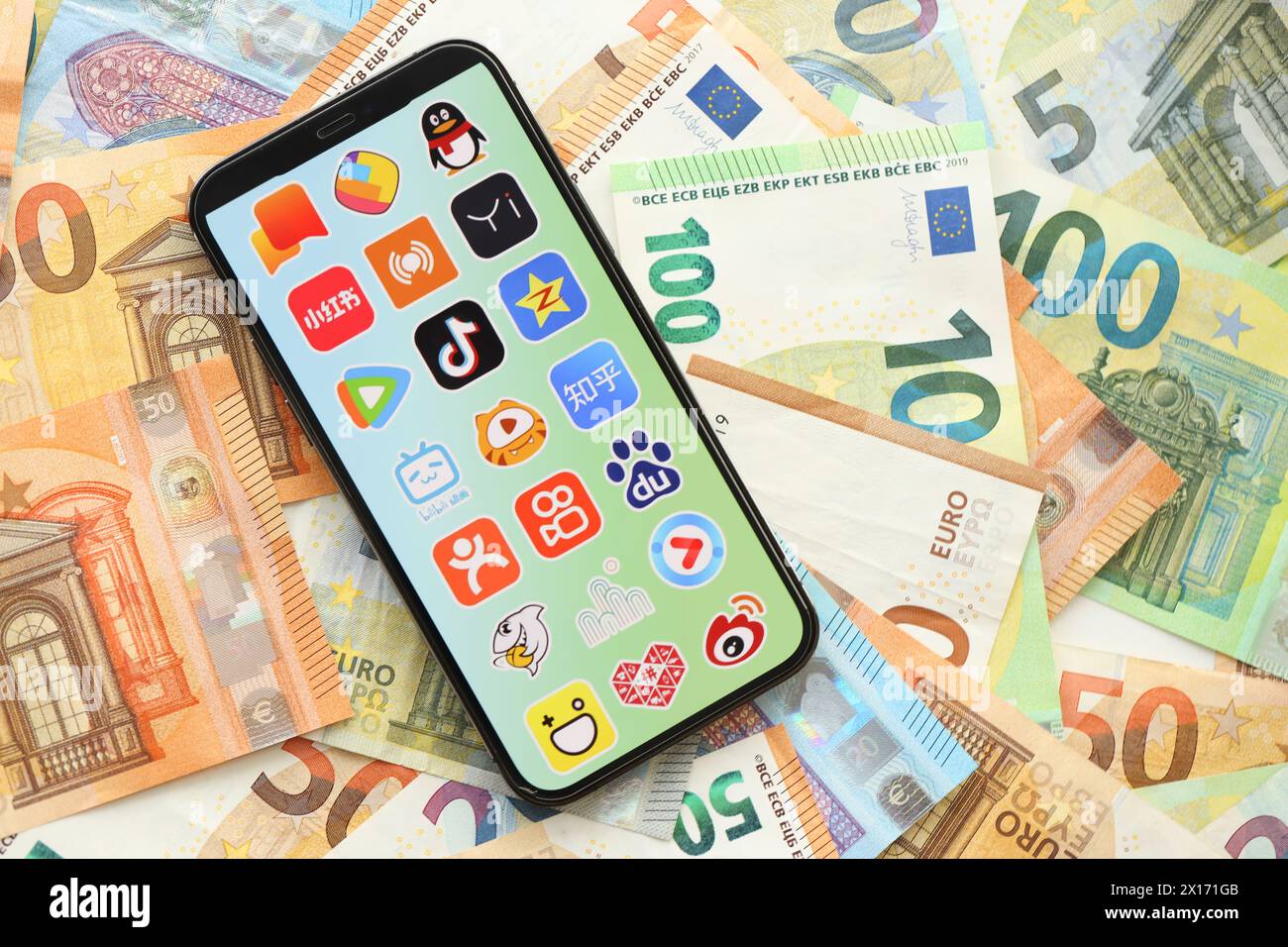 KIEW, UKRAINE - 1. APRIL 2024 auf vielen Euro-Geldscheinen finden Sie auf dem Smartphone-Bildschirm ein Symbol für asiatische Apps. IPhone-Display mit App-Logo mit Euro-Banknoten in europäischer Währung Stockfoto