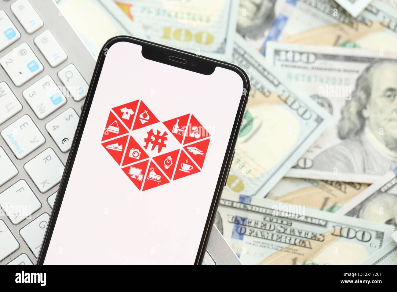 KIEW, UKRAINE - 1. APRIL 2024 Pinduoduo-Symbol auf dem Smartphone-Bildschirm auf vielen usd-Geldscheinen. IPhone-Display mit App-Logo und Dollarscheine mit weißer Tastatur Stockfoto