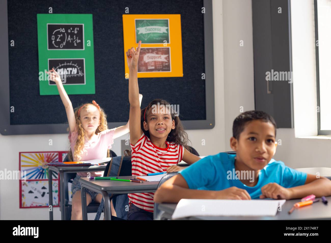 In der Schule heben verschiedene junge Schüler im Klassenzimmer die Hände, die darauf begierig sind, zu antworten Stockfoto