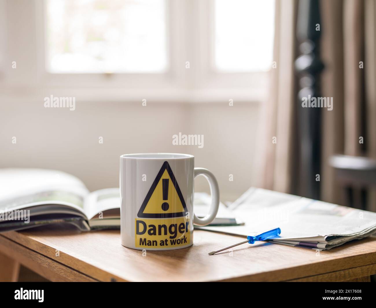 Becher "Danger man at Work" auf dem Tisch mit Schraubendiver und Zeitung Stockfoto