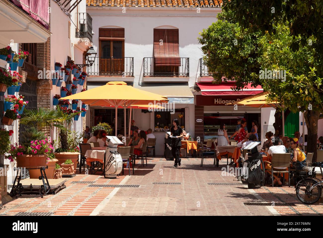 Die Menschen genießen eine gemütliche Terrasse auf einem Platz mit Geschäften und Restaurants auf dem Plaza de los Naranjos in der Altstadt von Marbella. Stockfoto