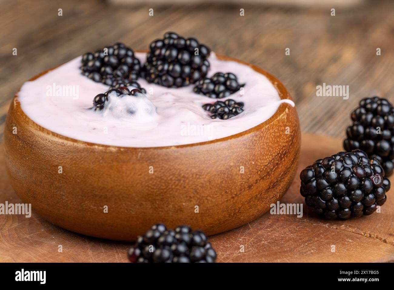 Rosafarbener Joghurt mit Beeren mit brombeergeschmack, Joghurt in einer Holzschale mit Reifen Brombeeren Stockfoto