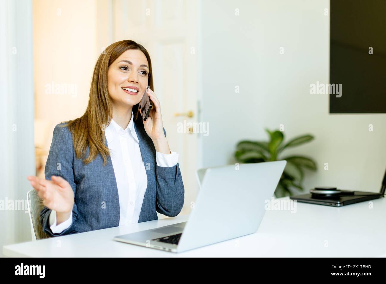Geschäftsfrau spricht über Dinge auf ihrem Smartphone und bewegt sich in ihrem modernen Bürobereich anschaulich. Stockfoto