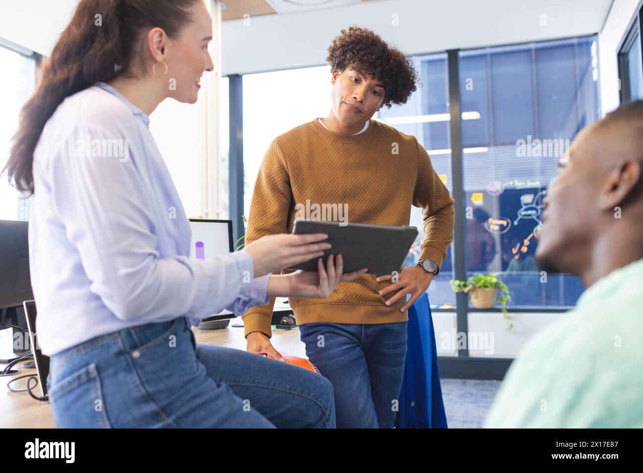 Ein vielseitiges Team diskutiert über ein Tablet, steht im Büro Stockfoto