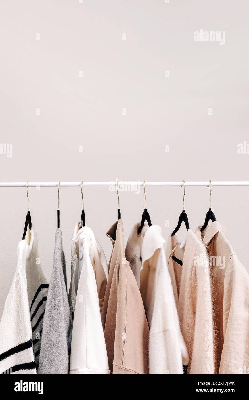 Beige und weiß gefärbte Garderobe, weibliche Kleidung an den Kleiderbügeln, Hemden und Pullover Stockfoto