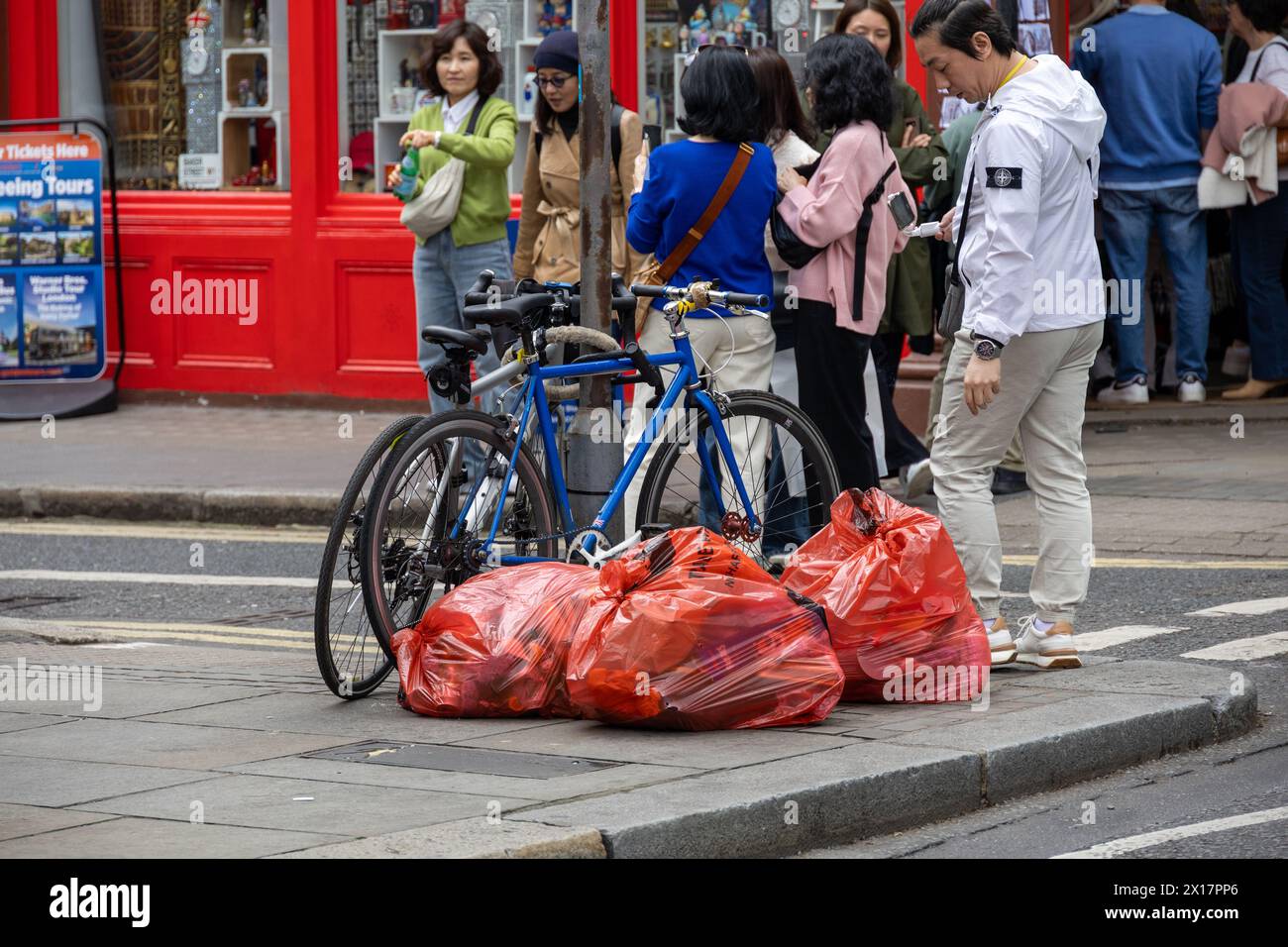 Londoner Straßenszene an einem Frühlingnachmittag, die das tägliche Leben und die urbane Aktivität mit Fußgängern, Fahrrädern und roten Müllsäcken auf dem Bürgersteig zeigt. Stockfoto