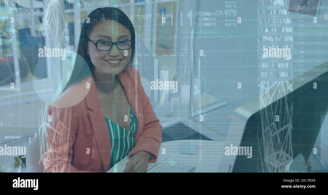 Über eine junge Geschäftsfrau mit birassischer Herkunft, die an einem Computer arbeitet und in die Kamera lächelt Stockfoto